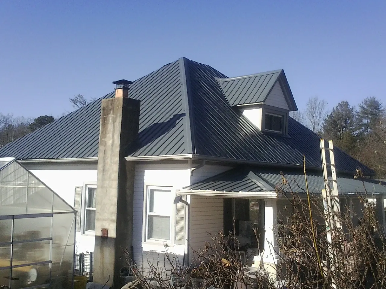 Dark blue standing seam metal roof on a white farmhouse with dormer — Slate & Tile Roof Repair by Roofing Brothers in Linesville