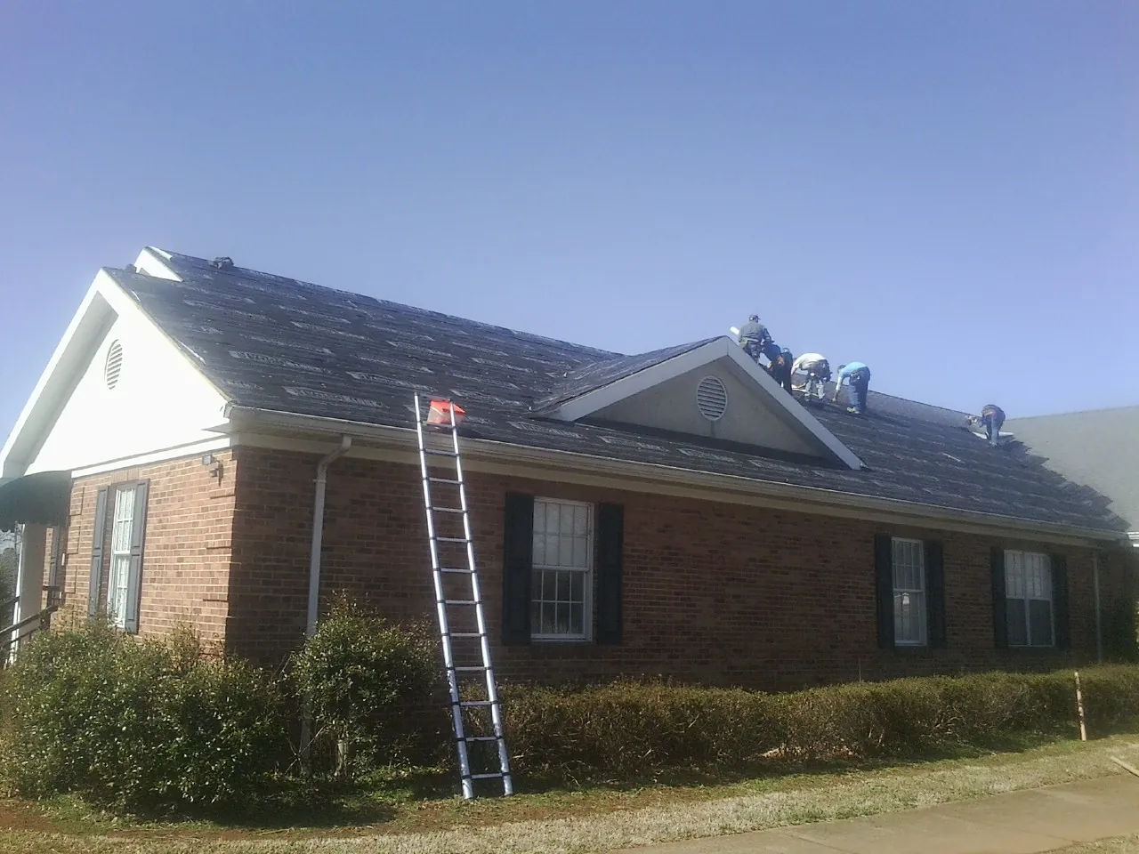 Crew tearing shingles off a brick ranch roof with a ladder set — Emergency Roof Repair work by our crew in Linesville