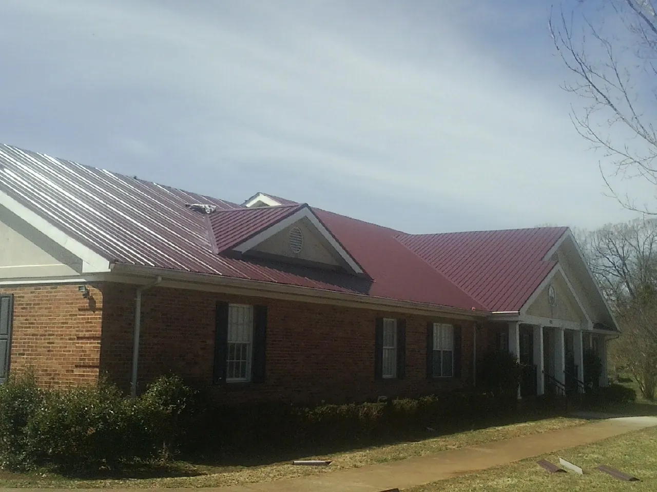 Red metal roof with gabled entries on a long brick building, from a Hail Damage Roof Repair job in Linesville