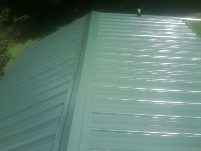New green metal panels meeting at the ridge of a roof — Flat Roof Repair work by our crew in Linesville