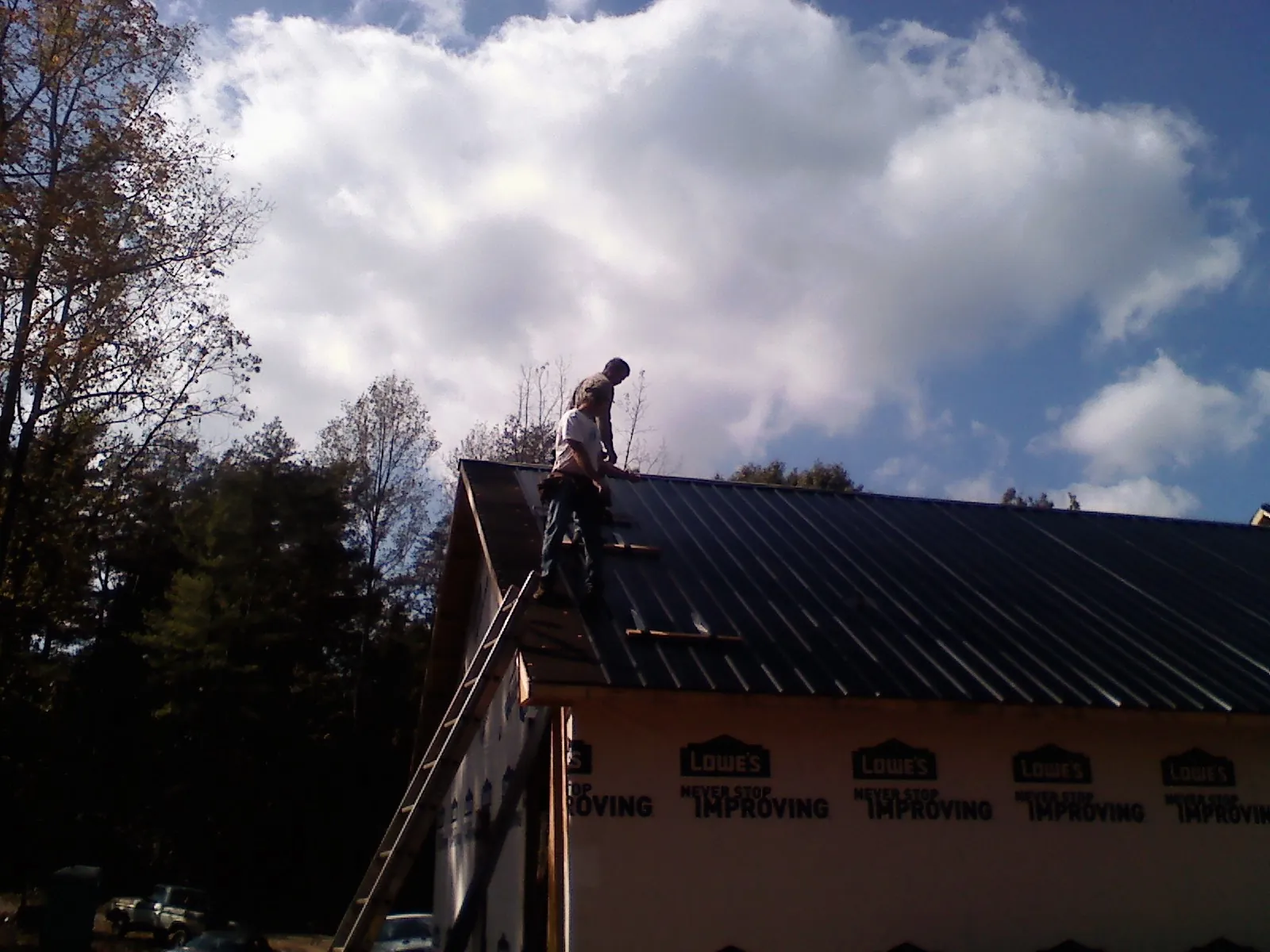 Roofer fastening dark metal panels high against a cloudy sky, from a Roof Inspection job in Linesville