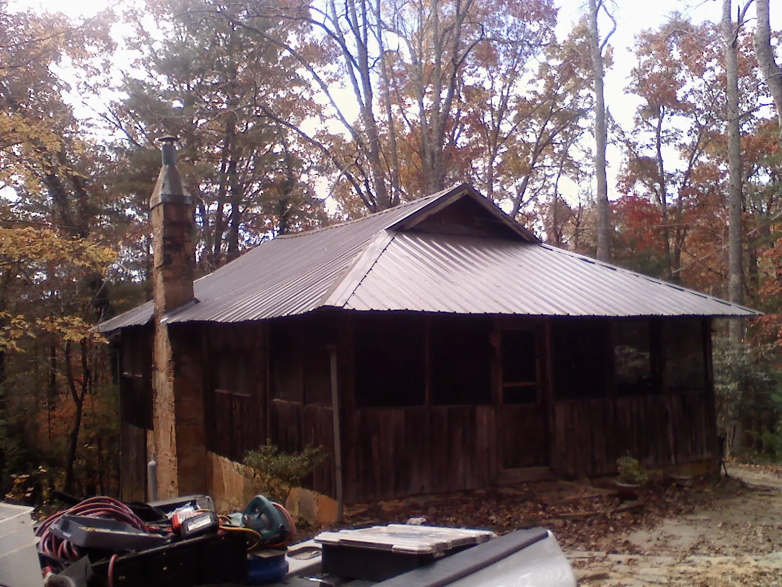 Brown metal hip roof on an old cabin with a stone chimney in Linesville