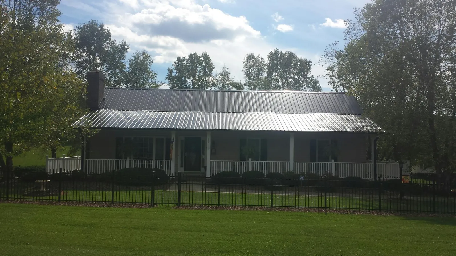 Gray metal roof on a brick ranch with a full width front porch — Gutter Guard Installation work by our crew in Linesville