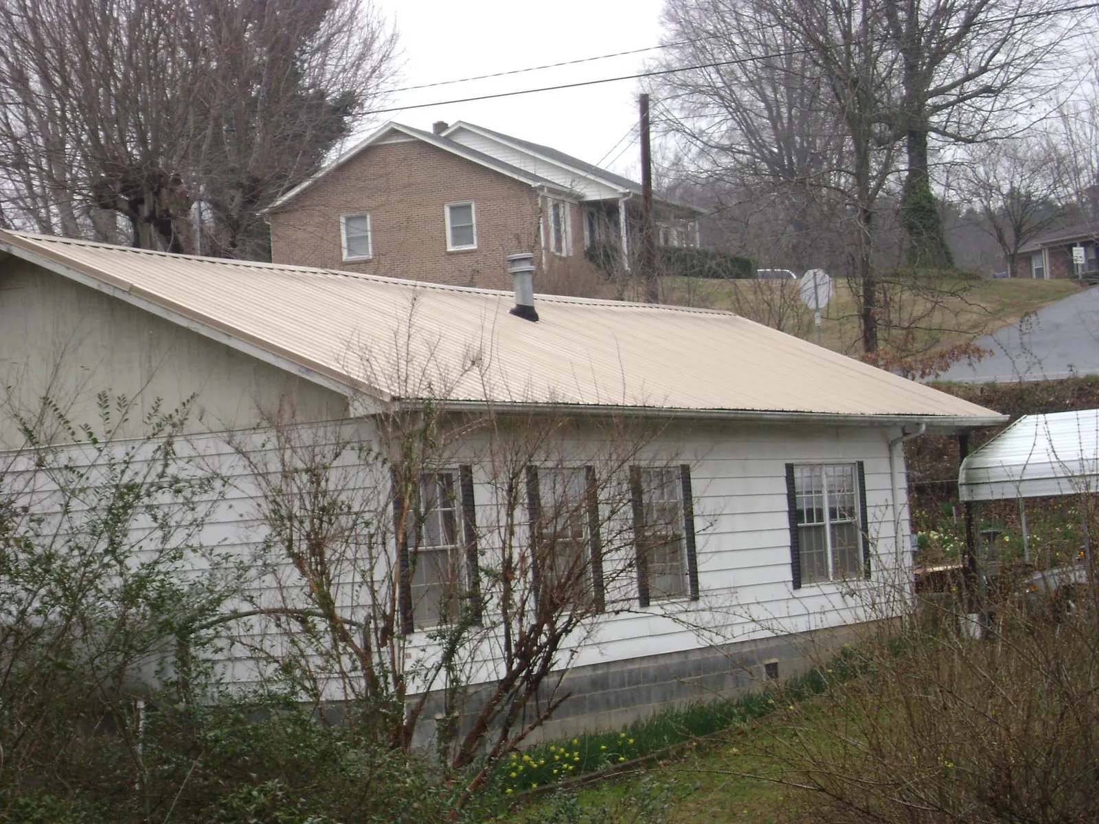 Tan metal roof on a white sided house set into a hillside — Commercial Roofing by Roofing Brothers in Linesville