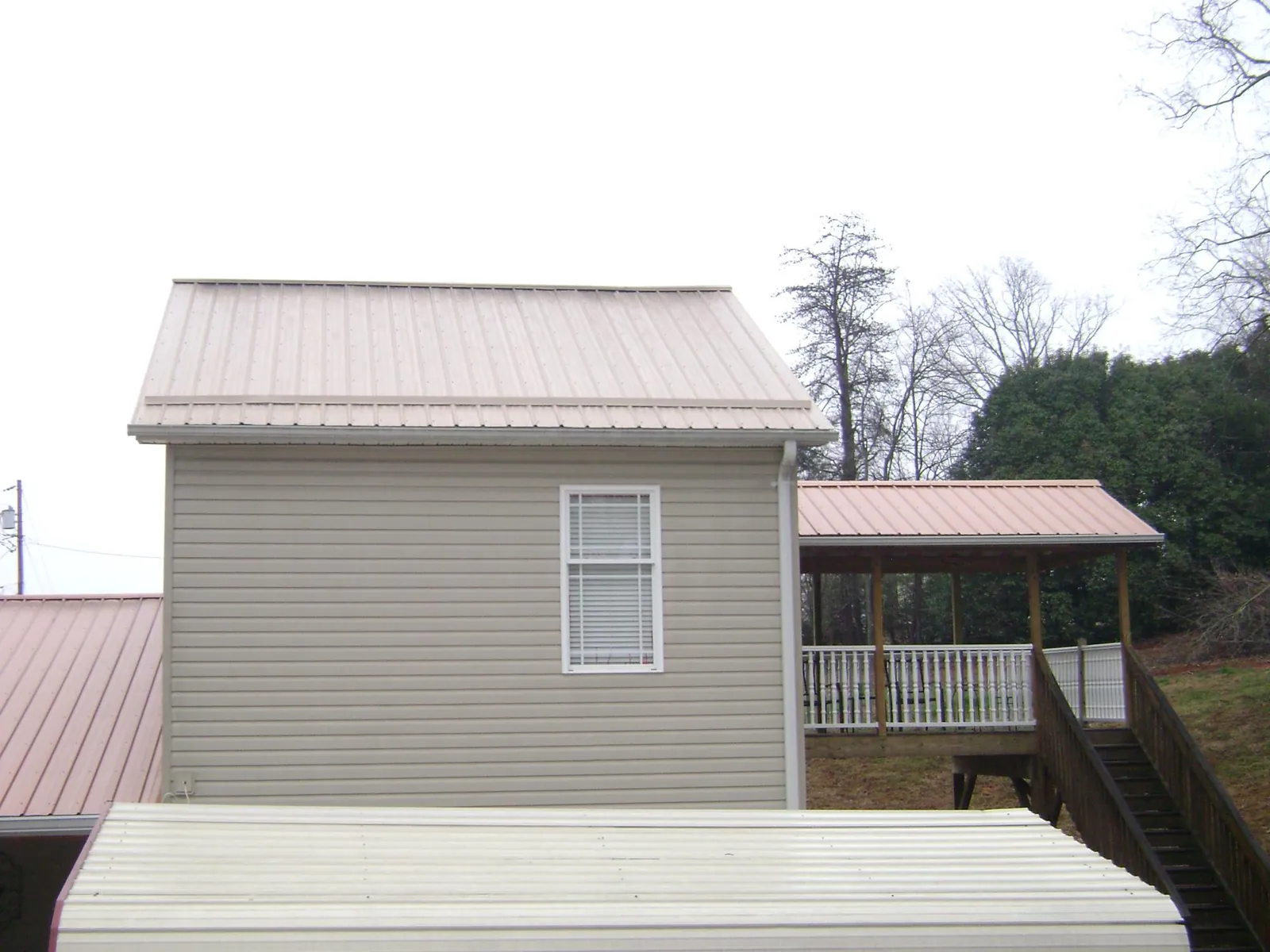 Tan metal roofs on a two story addition and attached porch, from a Roof Replacement job in Linesville